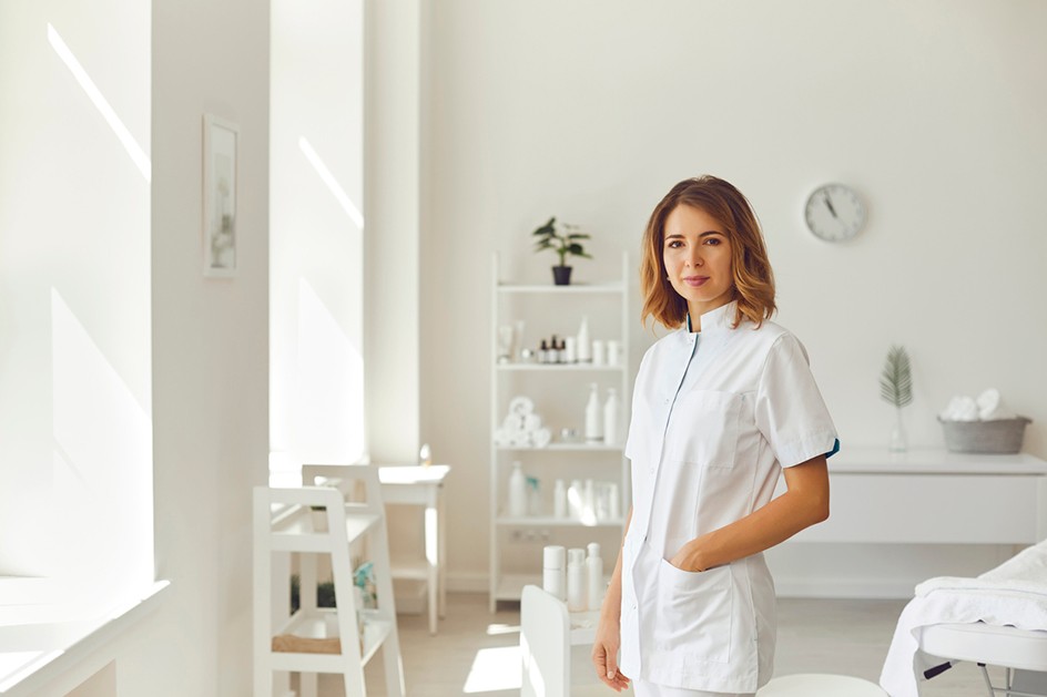 Female doctor wearing white scrubs in a therapy room smiling facing the camera