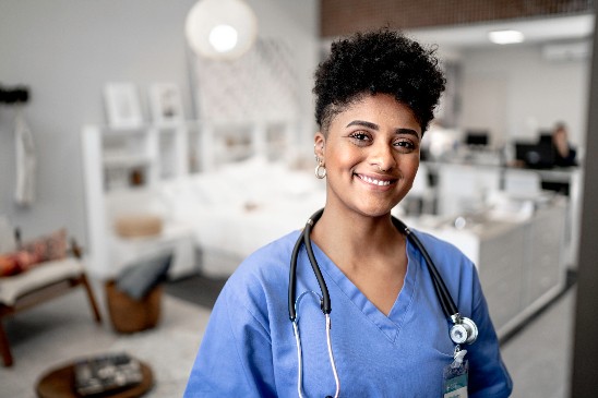 Female doctor wearing blue scrubs facing the camera smiling with a stethoscope around her neck